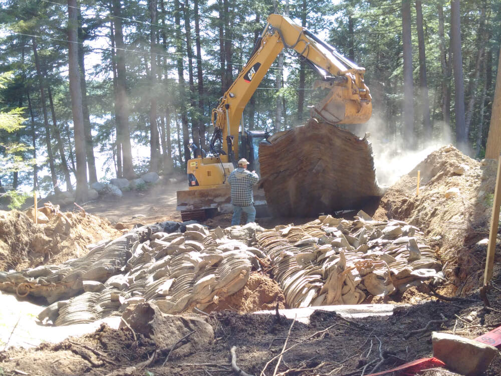 Excavator lifting rubber rock blasting mats into place prior to explosive bedrock removal in Township of Lake of Bays, Muskoka, Ontario.