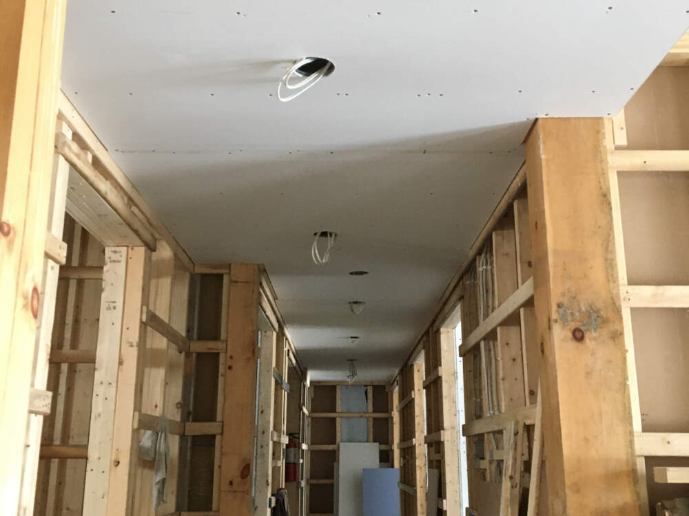 Gypsum board is installed in-place on the ceiling of a corridor with lighting electrical rough-in cables hanging for recessed light fixtures in a Lake Muskoka home building project.