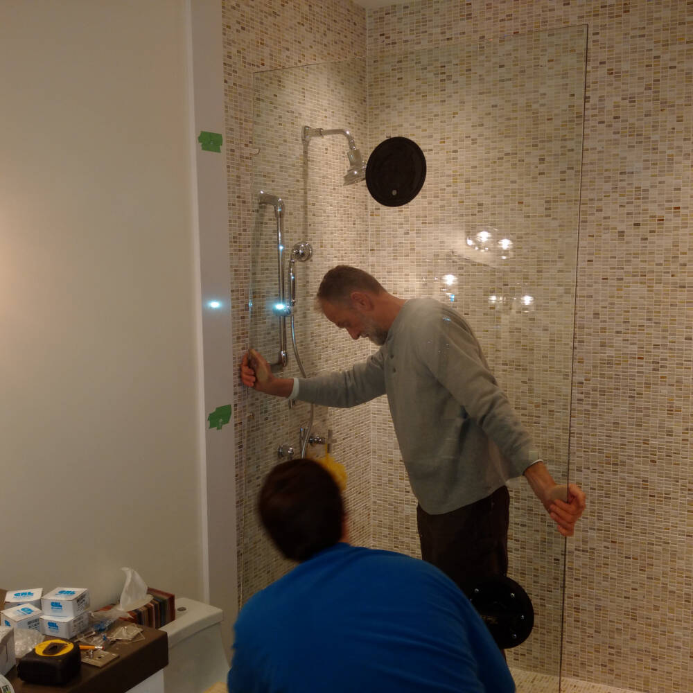Glazing contractor staff install a glass shower enclosure in a luxury bathroom built by skilled finish carpenters in Muskoka, Ontario.