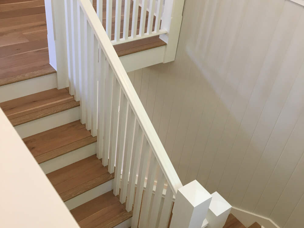 Red oak engineered hardwood flooring completes a custom staircase with white painted newel posts, balustrade and handrail in a custom home in Muskoka, Ontario.