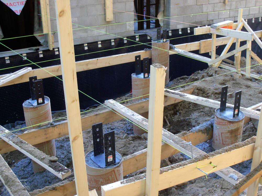 Batter boards and string lines are shown locating the centre of a pier foundation for a deck in Muskoka that has gotten underway following building permit approval.