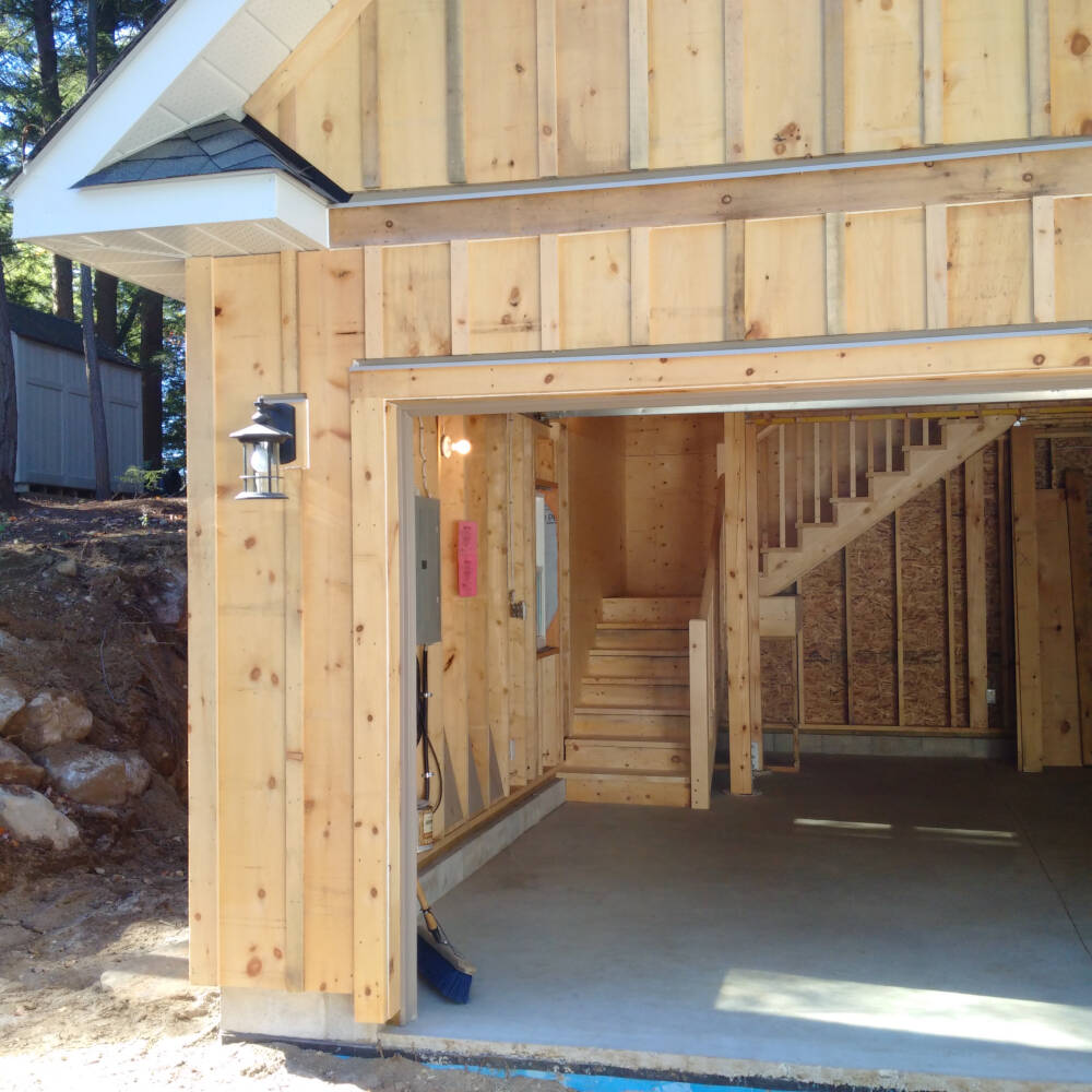 Details of a wood frame garage built by Classic Muskoka Homes in the Township of Lake of Bays are pictured, including stair case, window and door openings, 2x6 frame walls and vertical board and batten siding.