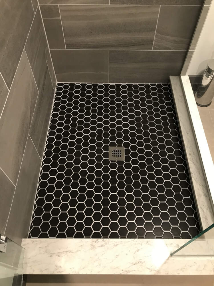 Black hexagonal ceramic tiles create an attractive pattern in contrast to the light grout colour on this shower floor.