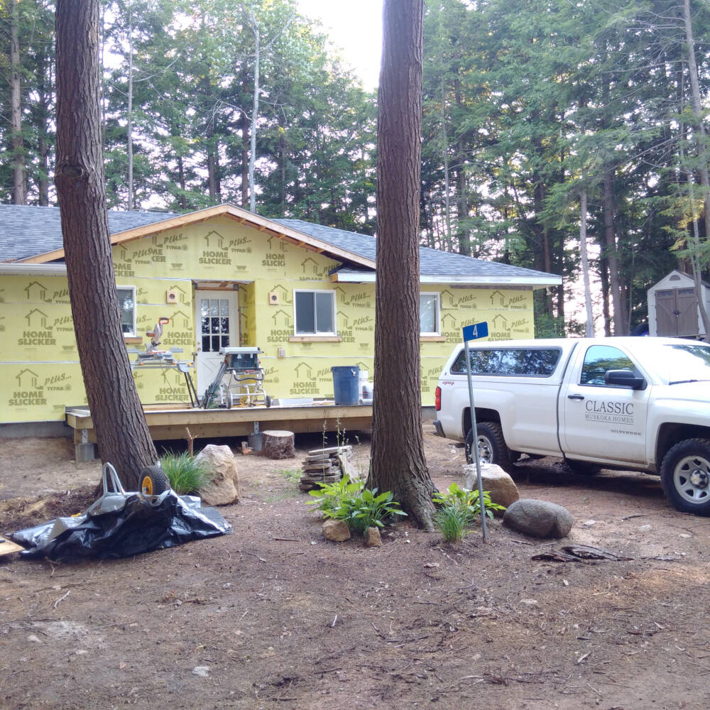 A Classic Muskoka Homes company truck is pictured in front of a Township of Lake of Bays cottage construction project on which siding installation is underway.
