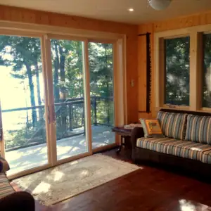 Wood flooring and wall paneling, large sliding glass doors, and wicker furniture decorate this Muskoka room.
