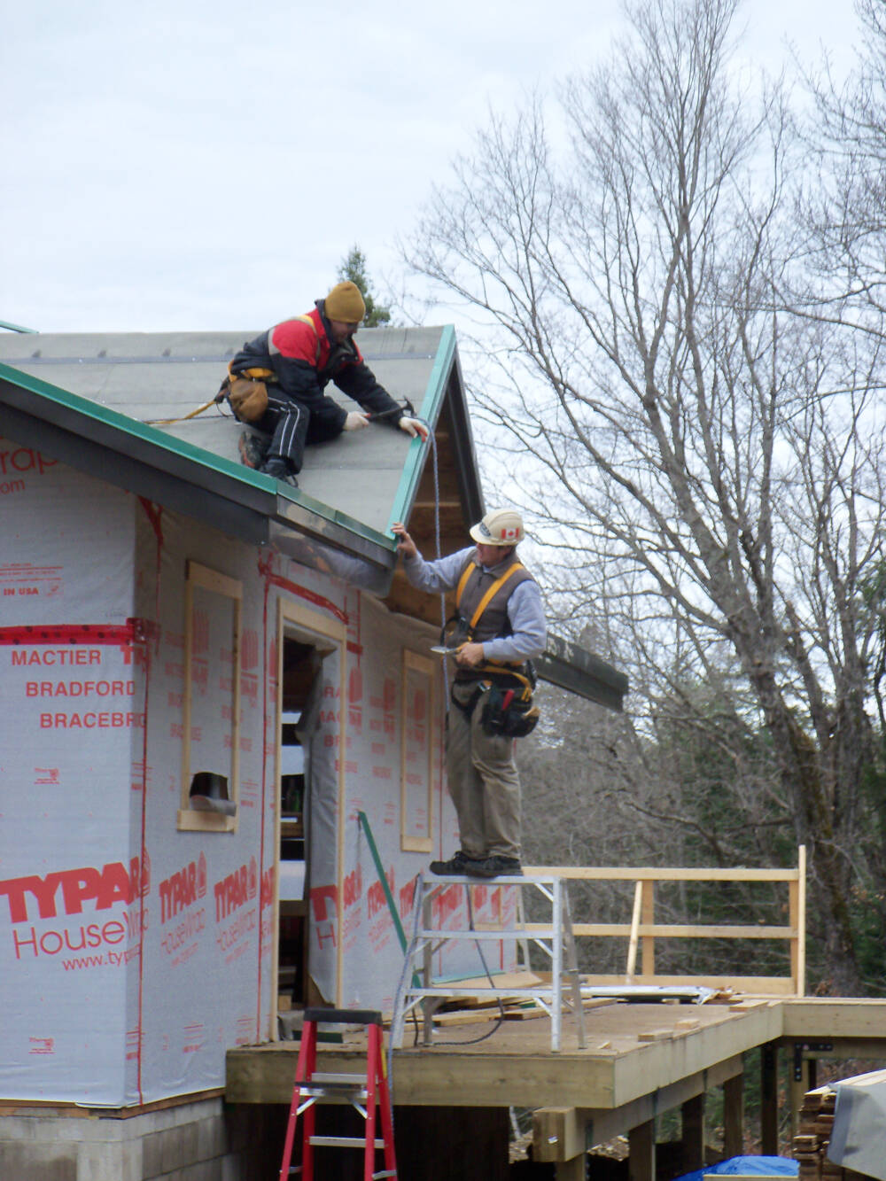 Two carpenters wearing hardhats and fall-arrest equipment install roofing materials on this Muskoka builder's construction project.