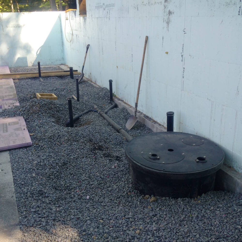 Drainage plumbing pipes and pump sump pit are installed prior to concrete placement and finishing for the basement floor of a cottage on Lake Muskoka.