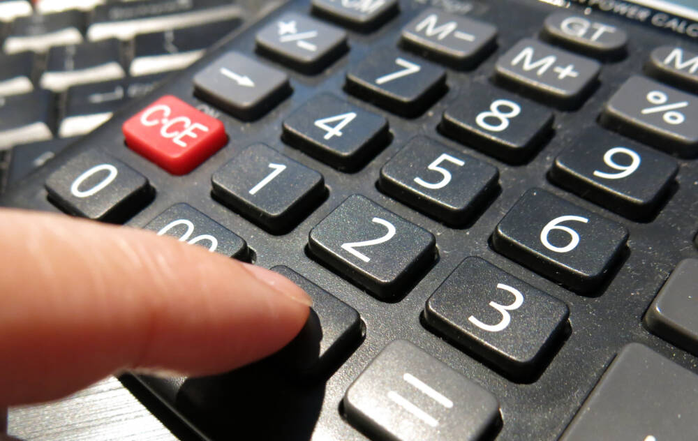 Calculator keyboard with finger engaged in a key-press action representing the act of construction work pricing.