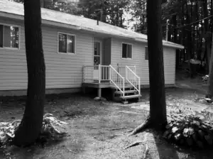 The original cottage exterior featured a very small enty deck, vinyl siding and a plain box building form prior to construction of this cottage plan.