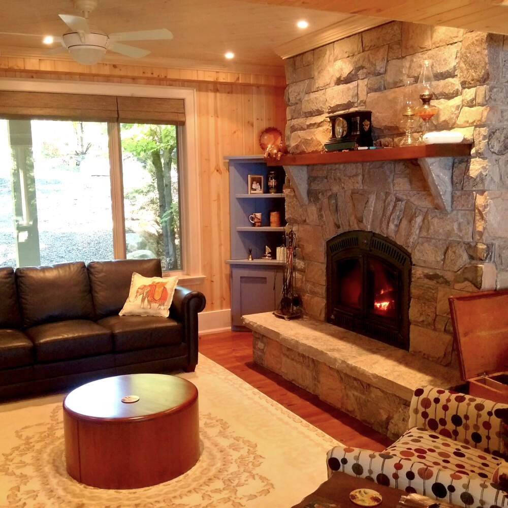 A cottage interior with wood paneling, stone fireplace and recessed ceiling lighting in Muskoka, Ontario.