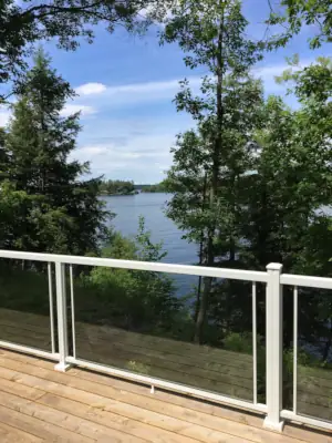 The blue water of Lake Muskoka is visible through the glass railing on the deck attached to this home design.