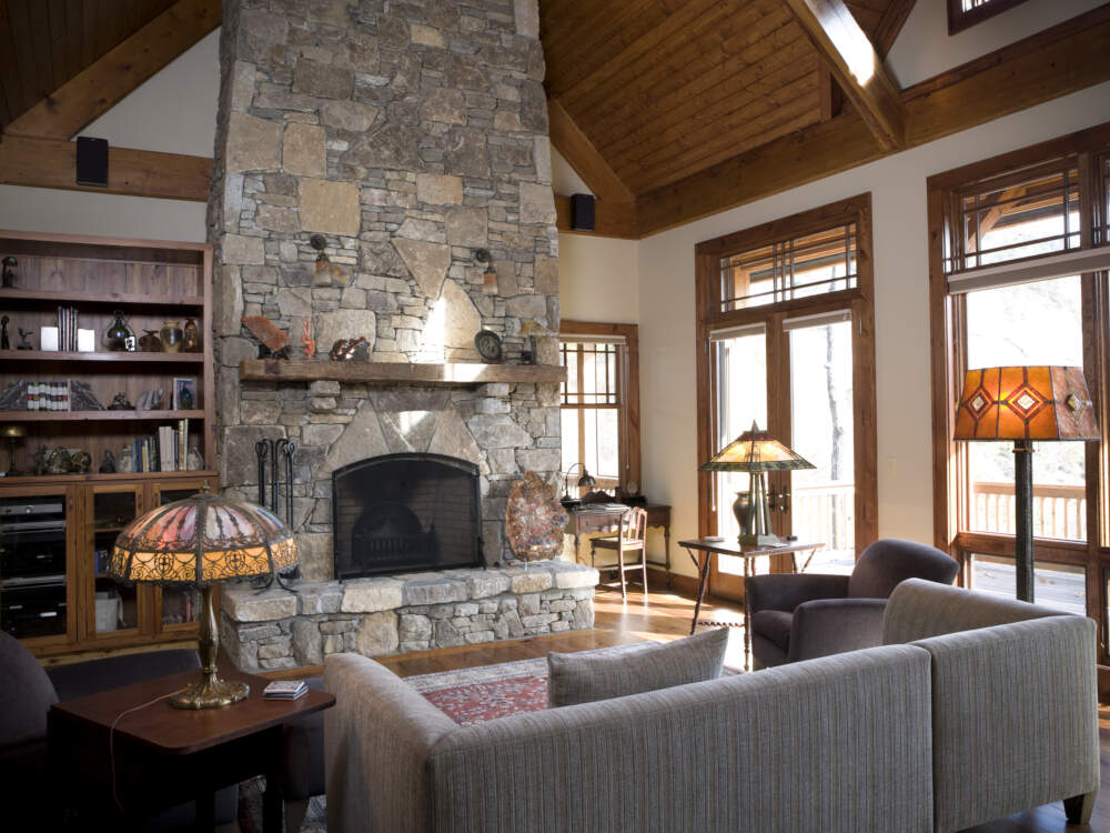 Lofty vaulted ceilings framed in solid douglas fir timber and finished with cedar decking contrast against white walls and stone fireplace in this mountain-style home design.