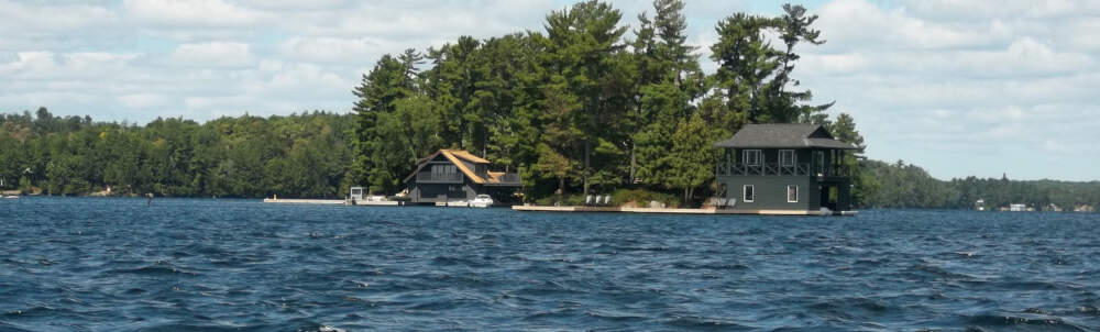 Bright sunlight shines on the deep blue water and forested shoreline of Lake Joseph in Muskoka - home to many classic Muskoka cottage and boathouse designs.