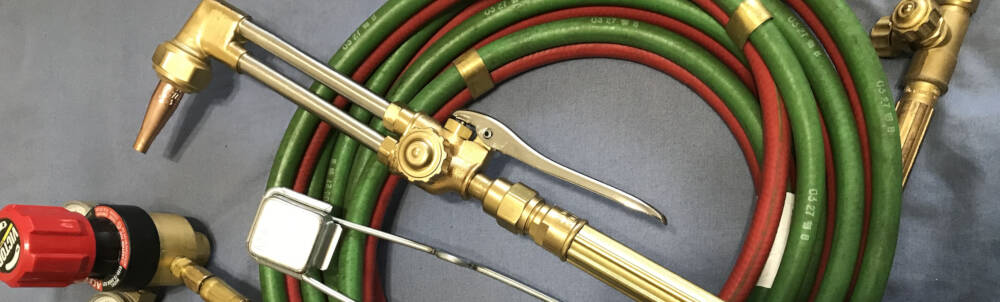 An oxy-acetylene cutting torch with fuel and oxygen hoses connected is shown to reference welded steel construction in Muskoka, Ontario.